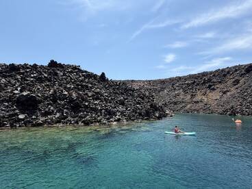 A young girl paddleboards in crystal-clear waters surrounded by a stunning rocky coastline, showcasing the beauty of outdoor adventures.