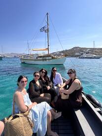 A group of friends enjoys a sunny day on a boat, surrounded by stunning turquoise waters — perfect for a memorable outing in Mykonos.