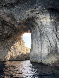 A stunning view of a natural rock arch framing the sky, showcasing the breathtaking coastline and crystal-clear waters — perfect for exploring hidden gems by boat.