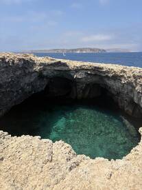 A stunning view of a secluded cove with crystal-clear waters and a sailboat in the distance, perfect for exploring the beautiful coastline.
