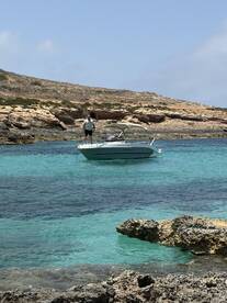 A person stands on a boat amidst stunning turquoise waters and rocky coastline, capturing the essence of a perfect day on the water.