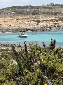 A scenic view of a speedboat anchored in crystal-clear waters, surrounded by rocky terrain and lush greenery, perfect for a day of exploration.