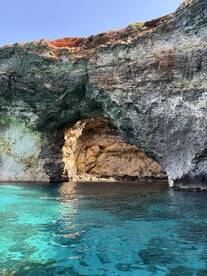A stunning view of a natural cave with crystal-clear turquoise waters, featuring a swimmer enjoying the picturesque scenery — a perfect highlight of a boating adventure.