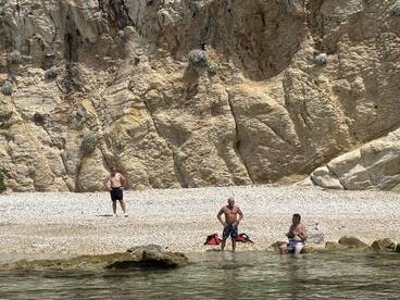 A group of men enjoys a sunny day at the beach, with rocky cliffs in the background, perfect for swimming and relaxation.