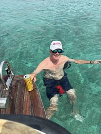 A man enjoys a refreshing drink while relaxing in the crystal-clear waters, capturing the essence of a perfect day on the water.