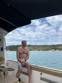 A man enjoys a moment of relaxation on the side of a boat, overlooking serene waters and lush landscapes — a perfect snapshot of leisure on the water.