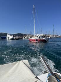 A picturesque view of a sailboat navigating through a marina, surrounded by various yachts under a clear blue sky.