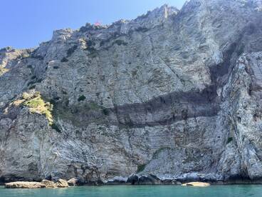 A stunning view of a rocky coastline, showcasing the natural beauty of the cliffs against the clear blue sky and tranquil waters — perfect for nature lovers and scenic boat tours.