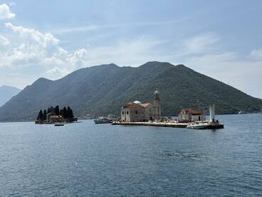 A picturesque view of an island with historic buildings set against a stunning mountainous backdrop, perfect for exploring coastal landmarks and enjoying scenic boat tours.