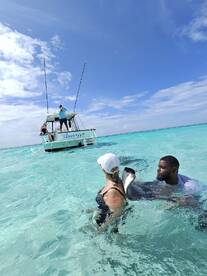 A woman interacts with a stingray in the clear waters, while a man assists her — an unforgettable wildlife experience in a tropical paradise.