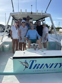 A cheerful group poses for a photo aboard the 'Trinity' in Grand Cayman, capturing a memorable moment on their boating adventure.
