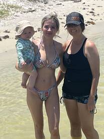 A joyful moment captured on the beach with a mother holding her child alongside a friend, perfect for family outings and beach adventures.