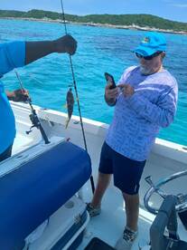 Two anglers enjoy a fishing trip in vibrant turquoise waters, showcasing their catch while capturing the moment on their phones — a perfect day on the water.