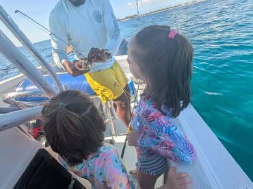 Two children watch in awe as an adult shows them a caught fish on a boat, creating a memorable fishing experience on the water.