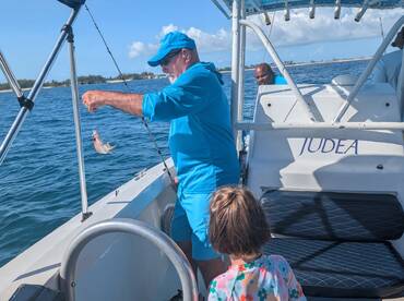 A joyful moment as a child watches an adult proudly display a freshly caught fish while fishing on a boat — a perfect family adventure on the water.