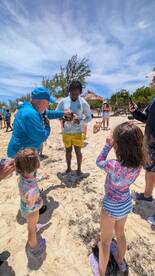 A group of people, including children, interact with a turtle on the beach, showcasing a memorable wildlife experience in a tropical setting.