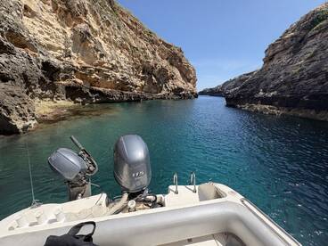 A scenic view of a boat navigating through a narrow cove, surrounded by stunning rocky cliffs and clear blue waters, perfect for exploring hidden gems along the coastline.