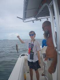 A young angler proudly displays his catch while fishing on a boat, surrounded by friends — a perfect moment of excitement and camaraderie on the water.