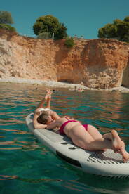 Two friends relax on a paddleboard in crystal-clear waters, enjoying a sunny day at the beach — a perfect moment for summer fun and relaxation.