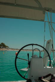 A close-up view of the helm and console of a boat, showcasing the steering wheel against a backdrop of clear turquoise waters and a sandy beach.