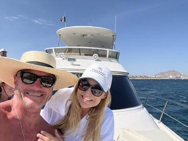 A cheerful couple poses for a selfie on a boat, enjoying a sunny day at sea — perfect for capturing memorable vacation moments.