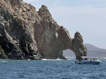 A scenic view of a boat cruising near the iconic rock formation at Cabo San Lucas, showcasing the stunning coastline and vibrant blue waters.