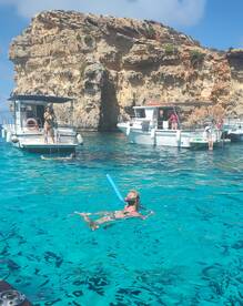A child enjoys swimming with a snorkel in crystal-clear waters, surrounded by boats and stunning rock formations — a perfect day for aquatic adventures.