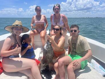 A joyful group celebrates a successful fishing trip on a boat, showcasing their catch and enjoying the sunny day on the water.