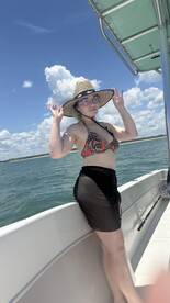 A young woman enjoys a sunny day on the boat, showcasing a fun summer vibe with clear skies and water in the background.