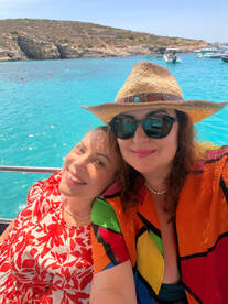 Two friends enjoy a sunny day on a boat, capturing a joyful moment against the backdrop of stunning turquoise waters and rocky cliffs — perfect for memorable beach outings.