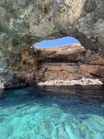 A stunning view of a natural cave along the coastline, with clear turquoise waters and people enjoying the scenery — a perfect spot for exploration and adventure.
