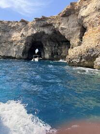 A stunning view of a boat navigating through a natural rock arch along a beautiful coastline, showcasing the breathtaking scenery of the area.