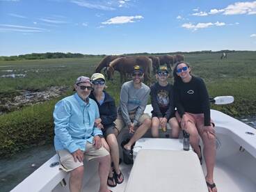 A family enjoys a day on the boat, with wild horses grazing in the background — a perfect blend of adventure and nature.