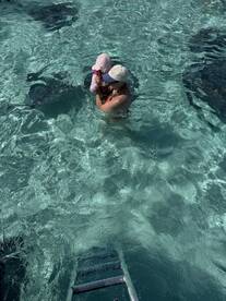 A mother holds her child while swimming with stingrays in crystal-clear waters, creating a memorable wildlife encounter perfect for family adventures.