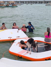 A lively group enjoys a fun day on floating mats in the water, complete with drinks and a playful dog — perfect for summer gatherings and beach parties.