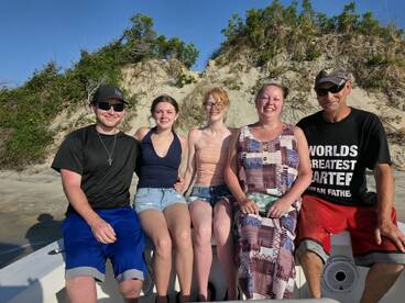 A cheerful group of family members poses together on a boat with a sandy beach backdrop, capturing a memorable moment during their day on the water.