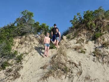 A group of friends enjoys a sunny day at the beach, climbing a sandy dune — perfect for outdoor adventures and fun in the sun.