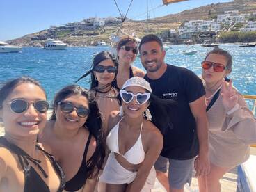 A joyful group of friends poses for a selfie on a boat in Mykonos, capturing the essence of summer fun and celebration on the water.