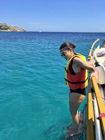 A woman in a life jacket prepares to jump into the crystal-clear ocean from the side of a boat, capturing the thrill of a summer adventure on the water.