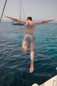 A man joyfully leaps into the crystal-clear waters from a sailboat, capturing the essence of summer fun and water activities.