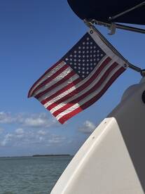A close-up of an American flag waving on a boat against a clear blue sky, showcasing the vessel's patriotic spirit while cruising on the water.