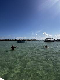 Guests enjoy a refreshing swim in clear waters at a sandbar, surrounded by boats — a perfect day for relaxation and fun on the water.