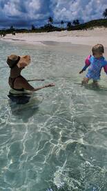 A joyful moment captured as a woman interacts with a child in the shallow waters of a beautiful beach, perfect for family fun and memorable summer days.