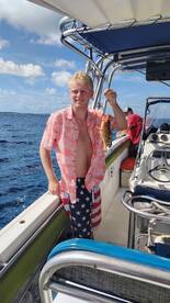 A young man proudly displays his catch while fishing on a boat, showcasing the excitement of a successful day on the water.