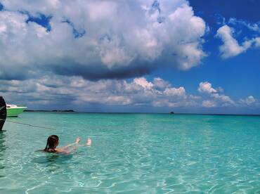 A person enjoys a refreshing swim in crystal-clear waters, with a boat anchored nearby, showcasing the beauty of a tropical getaway.