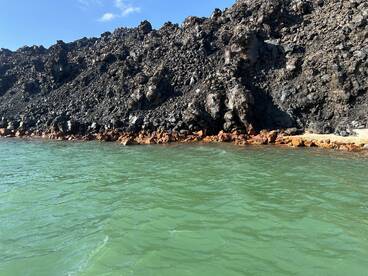A rocky shoreline with dark volcanic rock and green water, creating a unique natural landscape.