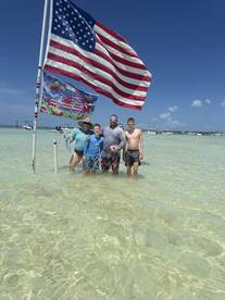 A family enjoys a fun day at the sandbar, posing with an American flag in the shallow waters — a perfect backdrop for memorable summer adventures.
