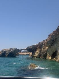 A stunning view of a natural rock arch along the coastline, with people enjoying the turquoise waters nearby — a perfect highlight of a boating adventure.