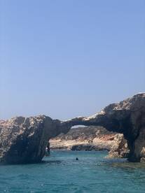 A stunning view of a natural rock arch with swimmers enjoying the clear waters nearby, showcasing the beauty of coastal adventures.