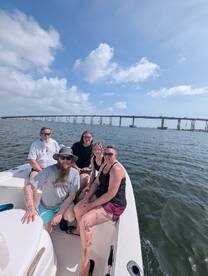A cheerful group of friends enjoys a day on the water, capturing the essence of fun and relaxation aboard their boat with a scenic bridge in the background.